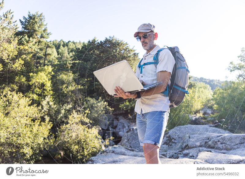 Älterer Mann mit Rucksack und Laptop Wanderer Reisender Browsen Natur benutzend Felsen felsig männlich Wanderung Ausflug Sonnenbrille reisen Apparatur Abenteuer