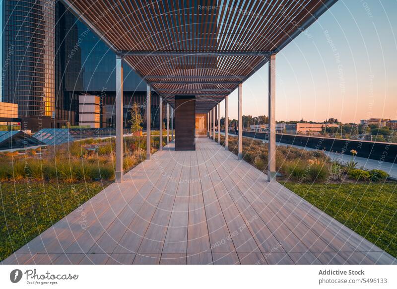Leerer Gehweg zwischen modernen Gebäuden mit Säulen im Tageslicht Laufsteg Gras Fluss Park Sonnenuntergang Buchse Außenseite Wasser Struktur Konstruktion