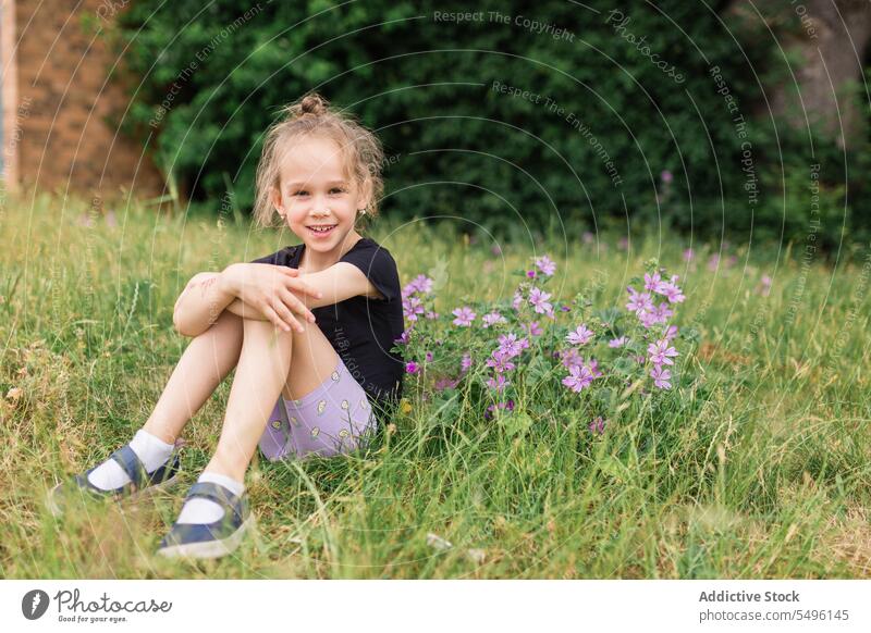 Lächelndes Mädchen auf grasbewachsenem Feld in der Nähe von Blumen Gras Natur Kind Glück Blütezeit bezaubernd Kindheit Sommer Flora heiter geblümt Umwelt Wiese