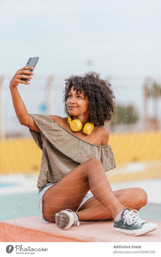 Lächelnde junge Frau mit Kopfhörern, die ein Selfie mit ihrem Smartphone macht Telefon benutzend zuhören Mobile Glück positiv Bank Gerät Straße genießen