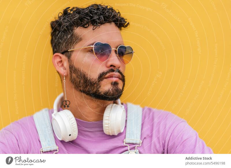 Bärtiger Mann mit Kopfhörern und Brille schaut vor gelbem Hintergrund weg nachdenklich ernst verträumt Porträt Headset Vollbart besinnlich benutzend Accessoire