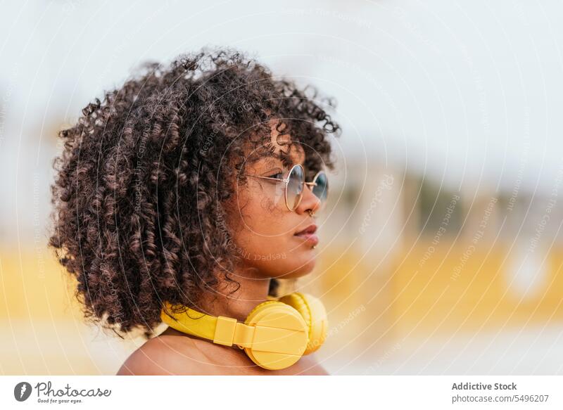 Junge Frau mit Kopfhörern und Brille Lockenfrisur schaut nach vorne Kopfschuss besinnlich Stil krause Haare Porträt Headset Audio trendy allein