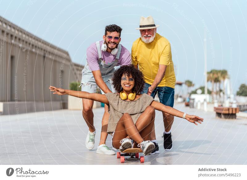 Fröhliche, bunt gemischte Freunde haben Spaß auf der Straße in der Stadt Mitfahrgelegenheit Skateboard Großstadt heiter Lächeln urban Glück Zusammensein positiv