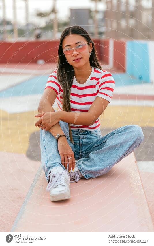 Junge asiatische Frau sitzt auf einer Steinbank verträumt nachdenklich besinnlich Windstille Bank allein lässig Brille sitzen friedlich trendy Inhalt attraktiv