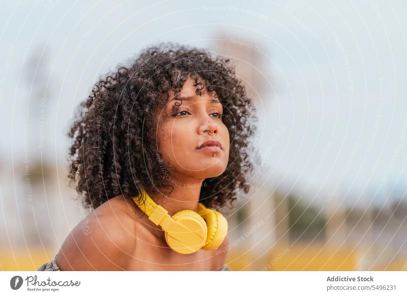 Junge Frau mit Kopfhörern und Lockenfrisur schaut weg Kopfschuss besinnlich Stil krause Haare Porträt Headset Audio trendy allein Menschliches Gesicht