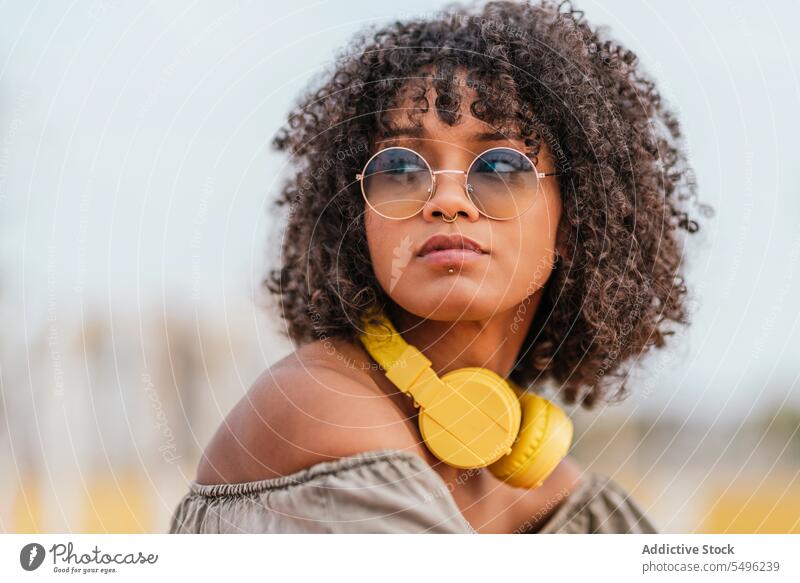 Junge Frau mit Kopfhörern und Brille Lockenfrisur schaut weg Kopfschuss besinnlich Stil krause Haare Porträt Headset Audio trendy allein Menschliches Gesicht