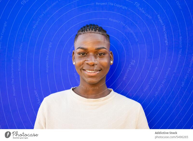Fröhlicher Teenager in weißem T-Shirt im Studio Junge selbstbewusst Lächeln Vorschein positiv Porträt Stil froh männlich Zopf jung Afroamerikaner ethnisch Glück