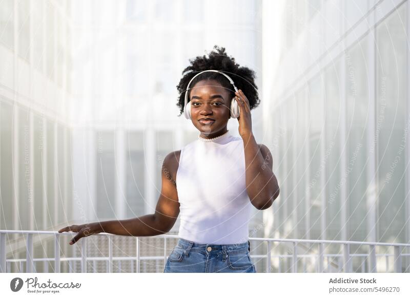 Schwarzes jugendliches Mädchen berührt Kopfhörer Teenager zuhören Musik Straße Gesang genießen Afro-Look positiv Apparatur Gerät Lächeln Wiedergabeliste schwarz