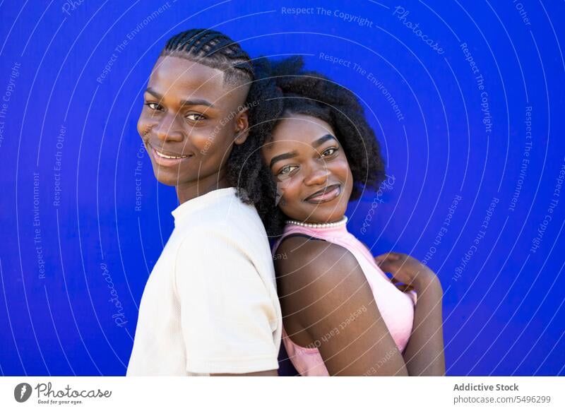 Fröhliches schwarzes Teenager-Paar, das sich Rücken an Rücken lehnt Afro-Look Zusammensein positiv Partnerschaft Frisur Vorschein Lächeln Porträt lässig