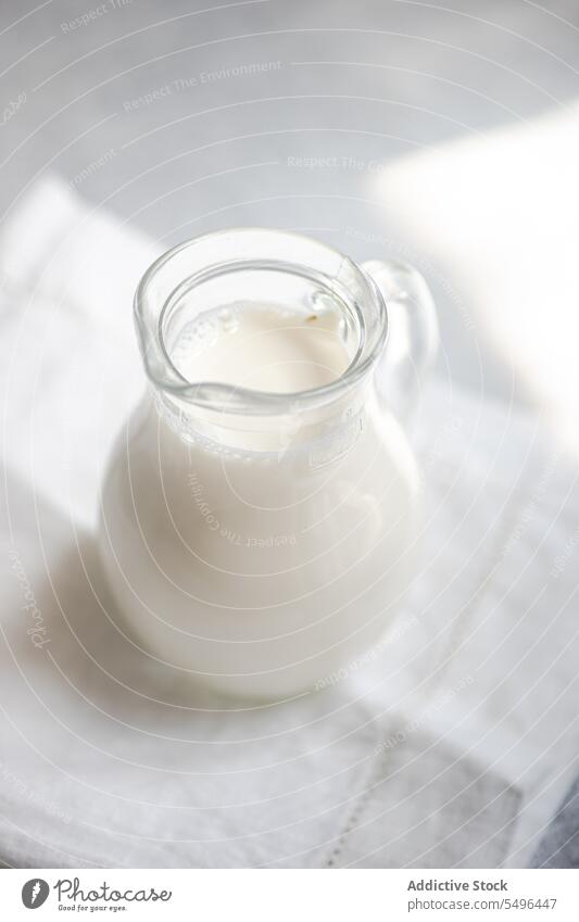 Rohmilch in Glasgefäß auf weißer, unscharfer Serviette roh Kuh melken rustikal trinken grau Oberfläche durchsichtig frisch Produkt Getränk Frühstück Ernährung