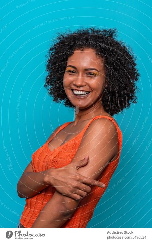 Lächelnde schwarze Frau in orangefarbenem Top schaut in die Kamera Mode Model schlank dunkles Haar krause Haare Afroamerikaner Outfit Stoff anhaben lässig
