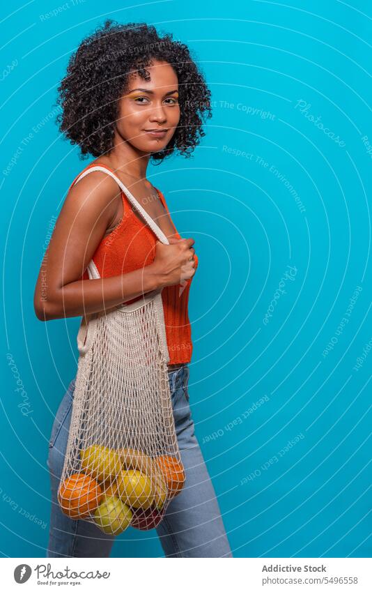 Glückliche schwarze Frau mit Obst Model Afro-Look Frisur führen Tasche Frucht Freude Afroamerikaner lässig Stil Outfit anhaben Stoff Top Jeanshose Jeansstoff