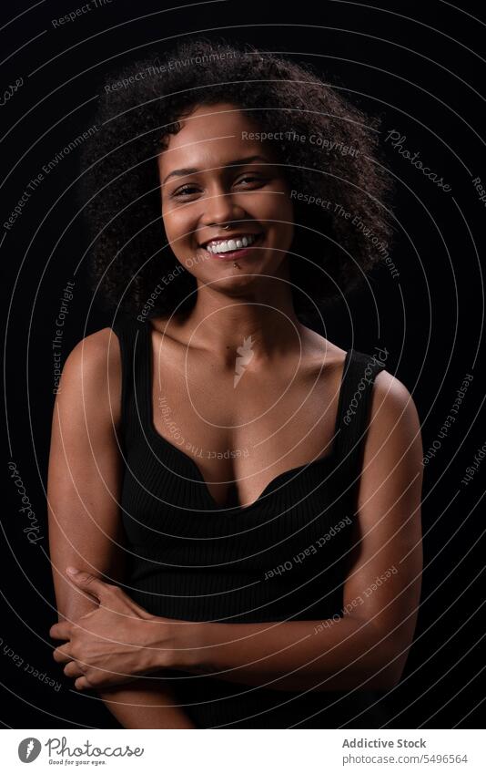 Lächelnde ethnische Frau schaut in die Kamera in einem dunklen Studio positiv Vorschein Freizeit sorgenfrei Glück Afro-Look krause Haare freundlich jung