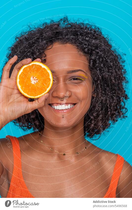 Lächelnde ethnische Frau, die ihr Auge mit einer Orangenscheibe bedeckt Glück orange Zitrusfrüchte Frucht Auge abdecken Scheibe Hautpflege Porträt jung