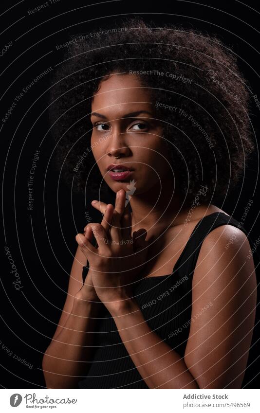 Nachdenkliche ethnische Frau schaut in die Kamera in einem dunklen Studio ernst Porträt Hände gefaltet Model Individualität tausendjährig besinnlich starren