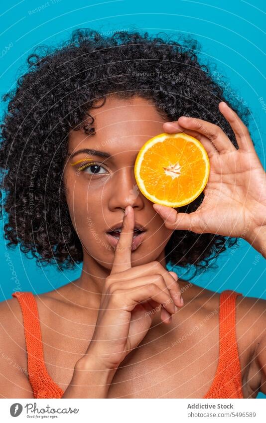 Frau bedeckt Auge mit Orangenscheibe und gestikuliert Stille Auge abdecken Porträt gestikulieren stumm orange Frucht Scheibe geheim Hautpflege Zitrusfrüchte