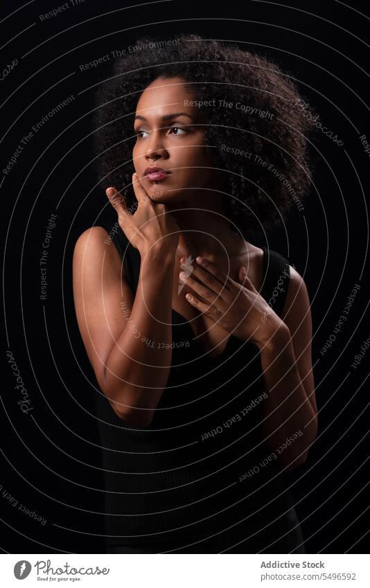 Nachdenkliche ethnische Frau berührt ihr Gesicht in einem dunklen Studio ernst Porträt Model Individualität tausendjährig besinnlich starren krause Haare