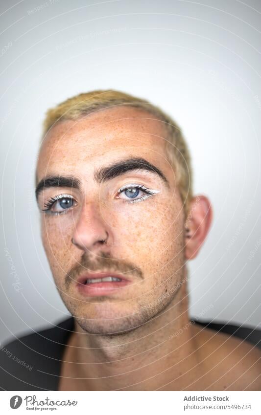 Selbstbewusster junger Mann mit blauen Augen in der Nähe einer weißen Wand im Zimmer Porträt Windstille Make-up Vorschein unrasiert Schnurrbart Kurze Haare