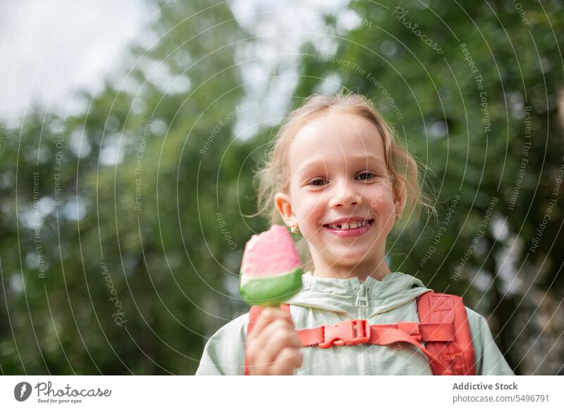 Mädchen mit Rucksack steht in der Nähe grasbewachsenen Feld und genießt Eis Kind Speiseeis Park Weg niedlich Kindheit grün bezaubernd Sommer süß sorgenfrei