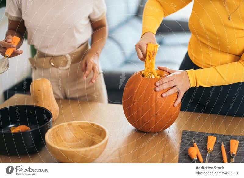 Anonyme junge Frauen stehen mit orangefarbenem Kürbis zu Hause Halloween Zellstoff ziehen Tisch hispanisch ethnisch Werkzeug Finger Schalen & Schüsseln Utensil