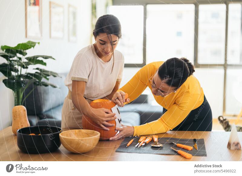 Junge ethnische Frauen stehen am Tisch mit Halloween-Papierdruck auf Kürbis Freund Wagenheber o Laterne Werkzeug kreativ vorbereiten zu Hause jung hispanisch