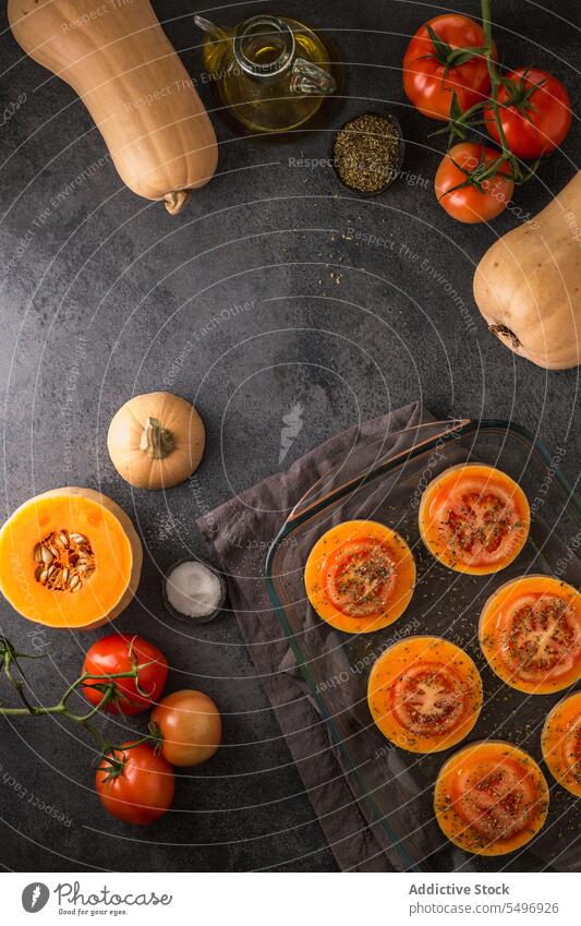 Ganzer und in Scheiben geschnittener Butternusskürbis und Tomaten auf Glasplatte Gemüse frisch Squash reif Kürbis organisch natürlich Lebensmittel Vitamin Küche