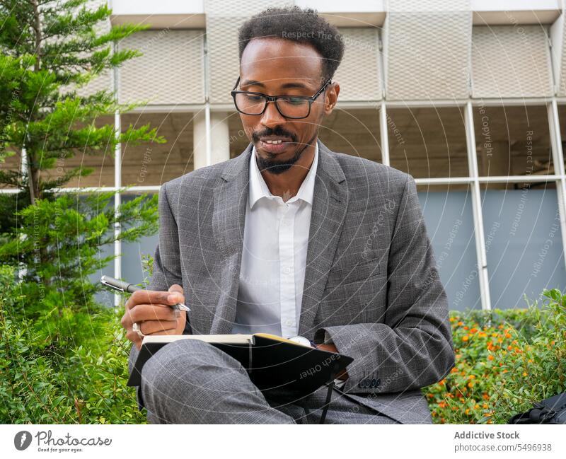 Schwarzer Mann schreibt in Notizbuch auf der Straße zur Kenntnis nehmen Großstadt Notebook schreiben Geschäftsmann Planer männlich Afroamerikaner Fokus urban