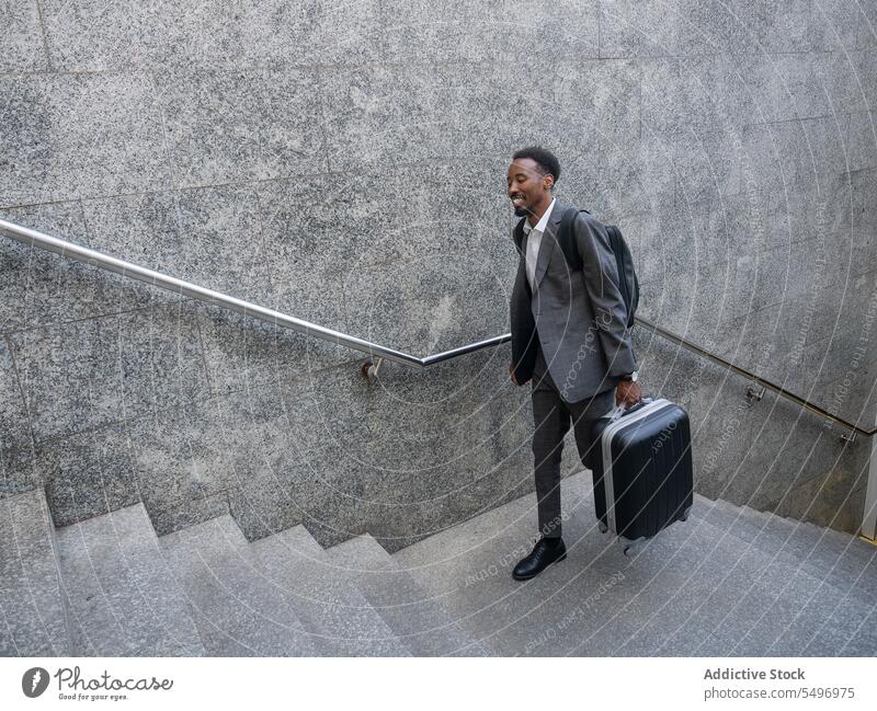 Fröhlicher schwarzer Mann mit Koffer geht eine Treppe hinauf nach oben unterirdisch Glück formal Spaziergang Treppenhaus Geschäftsmann männlich heiter Gepäck