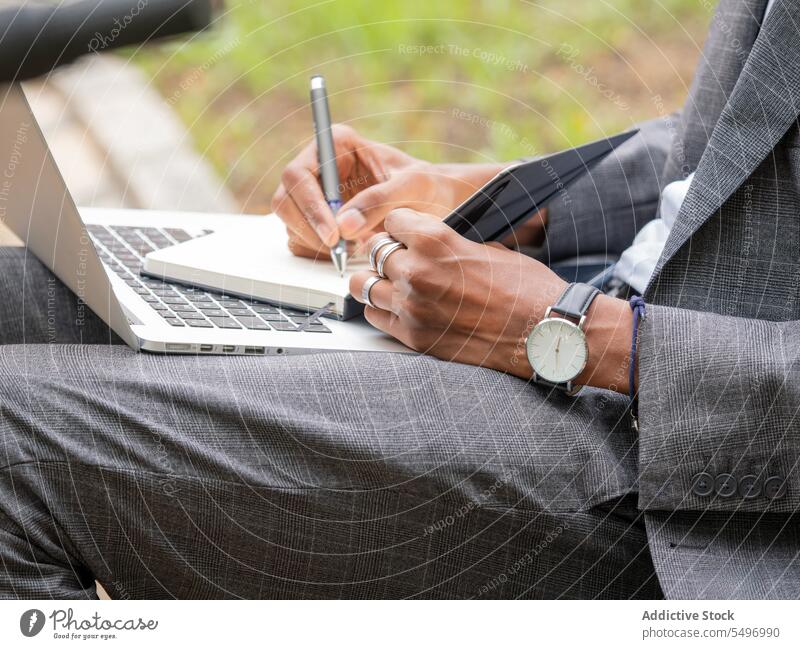 Unbekannter Geschäftsmann, der mit einem Stift in einen Notizblock schreibt, während er mit einem Laptop im Tageslicht sitzt zur Kenntnis nehmen Unternehmer
