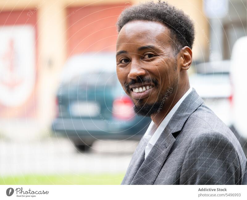 Fröhlicher junger schwarzer Geschäftsmann in formellem Anzug im Tageslicht sitzend Mann Straße selbstbewusst formal Lächeln heiter urban Automobil PKW männlich