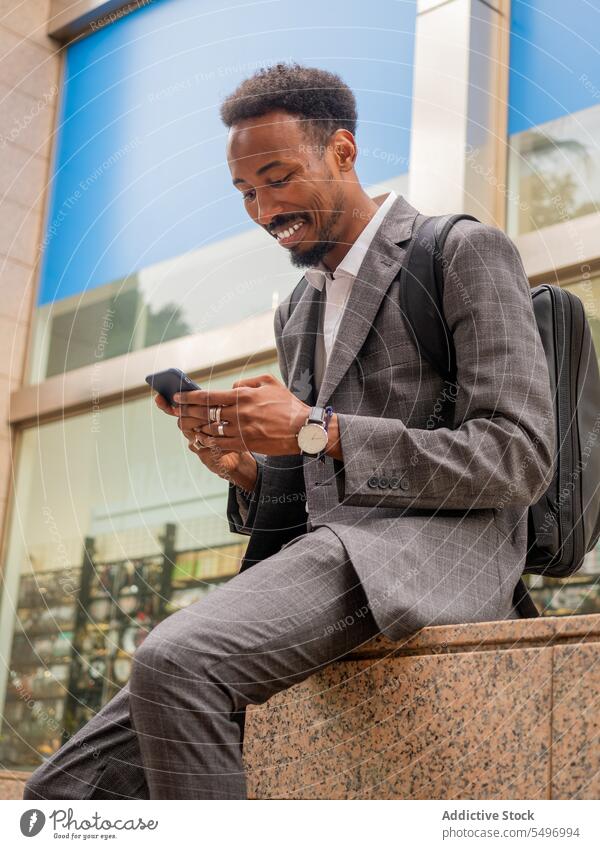 Glücklicher schwarzer gutaussehender Mann, der auf der Straße ein Mobiltelefon benutzt Geschäftsmann Unternehmer Smartphone Browsen benutzend Mitarbeiter Texten