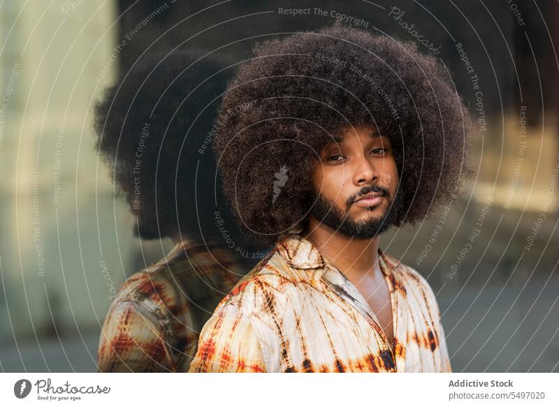 Mann mit Afrofrisur schaut in die Kamera gegen eine verspiegelte Wand Straße Aussehen Spiegel Vorschein krause Haare Reflexion & Spiegelung Afro-Look Frisur