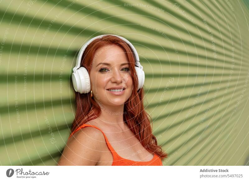 Glückliche Frau hört Musik an einer grünen Wand zuhören Kopfhörer Lächeln heiter benutzend Freizeit sorgenfrei lässig jung Freude Lifestyle modern Gerät Gesang