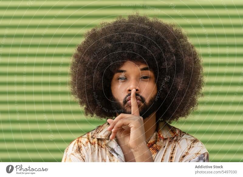 Schwarzer Mann, der in der Nähe der Wand eine Geste des Schweigens macht Porträt stumm gestikulieren shh Afro-Look ernst geheim stumm schalten krause Haare