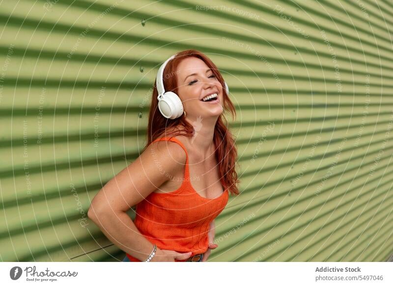 Glückliche Frau hört Musik an einer grünen Wand zuhören Kopfhörer Lächeln heiter benutzend Tanzen Freizeit sorgenfrei lässig jung Freude Lifestyle modern Gerät