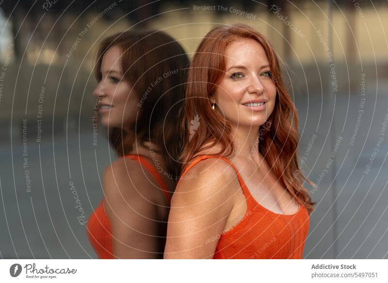 Lächelnde rothaarige Frau, die an einer Glaswand steht Porträt reflektieren Reflexion & Spiegelung Vorschein Individualität anlehnen Gebäude Straße