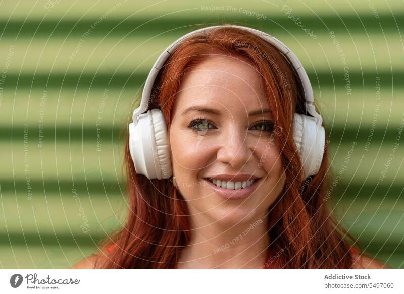 Glückliche Frau hört Musik an einer grünen Wand zuhören Kopfhörer Lächeln heiter benutzend Tanzen Freizeit sorgenfrei lässig jung Freude Lifestyle modern Gerät