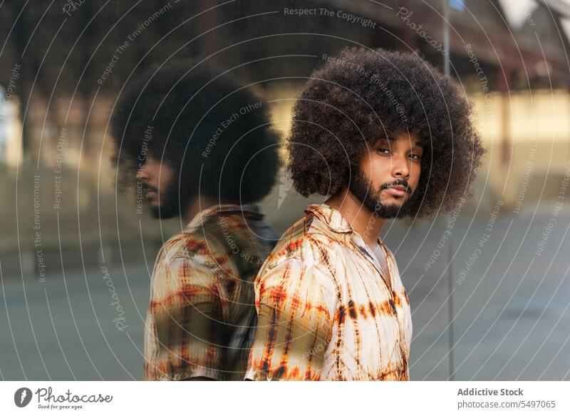 Mann mit Afrofrisur schaut in die Kamera gegen eine verspiegelte Wand Straße Aussehen Spiegel Vorschein krause Haare Reflexion & Spiegelung Afro-Look Frisur