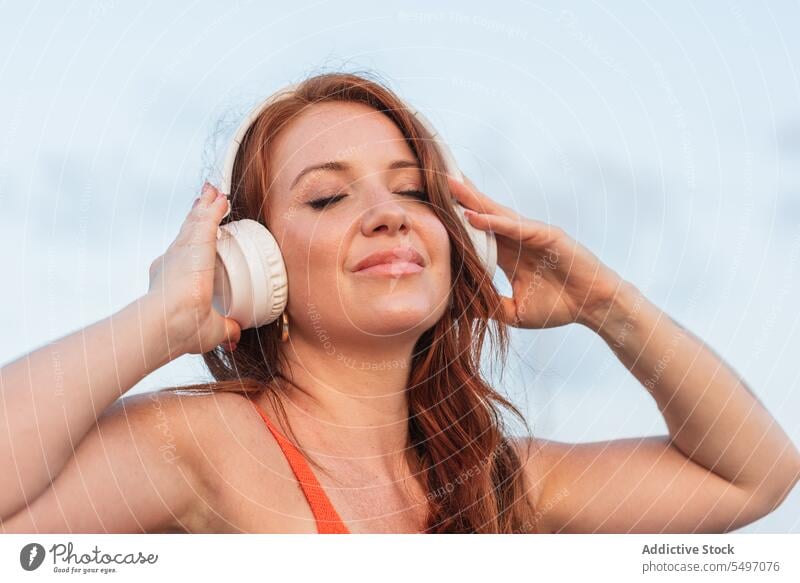 Junge Frau, die mit Kopfhörern Musik hört zuhören Drahtlos benutzend genießen positiv Lächeln Apparatur Gerät Gesang jung Audio Klang Melodie sorgenfrei Glück