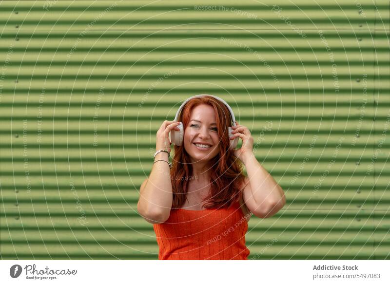 Glückliche Frau hört Musik an einer grünen Wand zuhören Kopfhörer Lächeln heiter benutzend Freizeit sorgenfrei lässig jung Freude Lifestyle modern Gerät Gesang