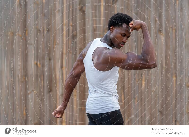 Starker schwarzer männlicher Athlet zeigt Muskeln auf der Straße Mann Bodybuilder Bizeps stark muskulös selbstbewusst Training Kraft Stärke Sportler jung