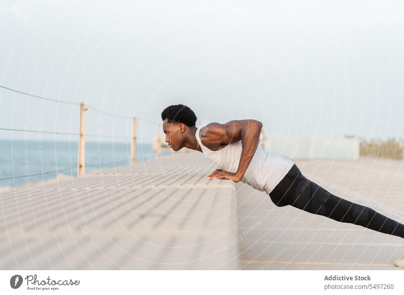 Schwarzer Mann macht Liegestütze an einer Böschung hochschieben Stauanlage MEER Training Übung Sport Sportbekleidung Wasser männlich Afroamerikaner Gesundheit