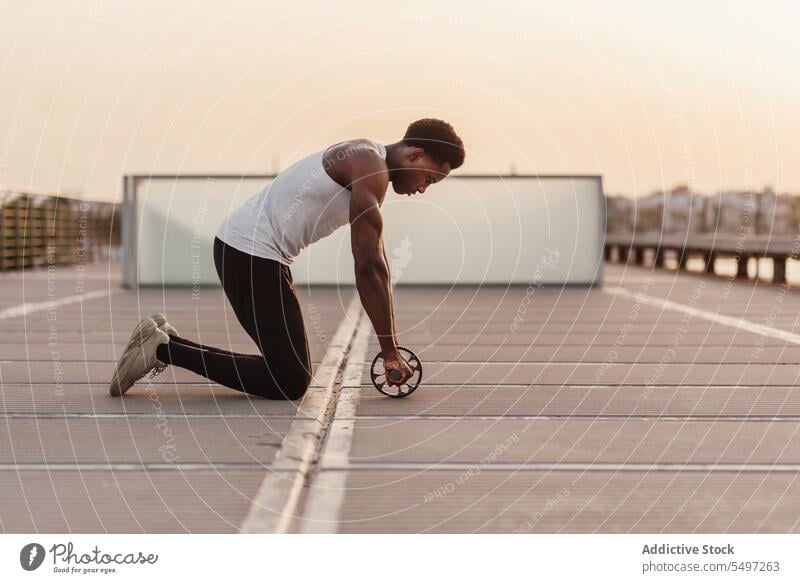 Fokussierter schwarzer Sportler bei Übungen mit einer Bauchmuskelrolle Mann Stauanlage Training Abend MEER männlich Unterleib Bauchmuskeln Sportbekleidung Kraft