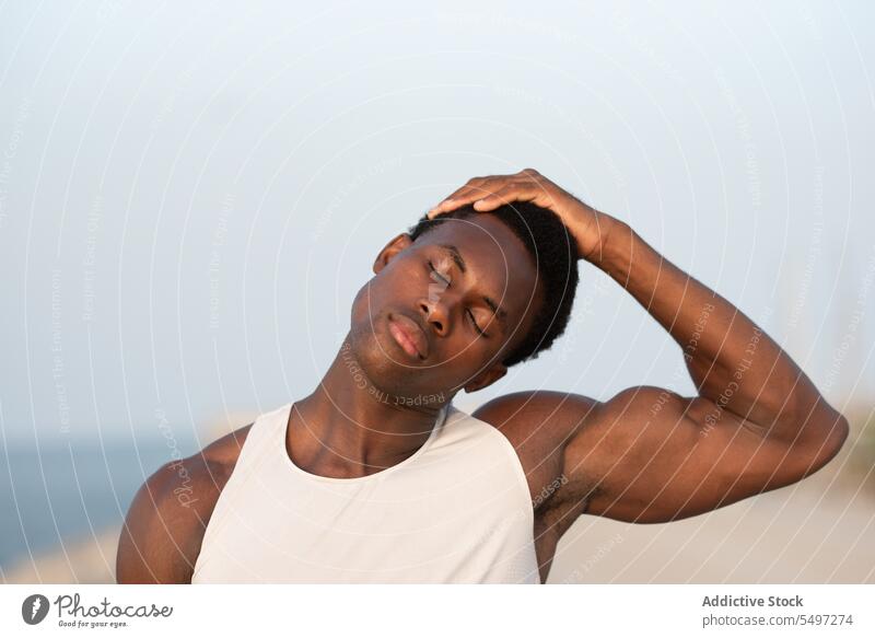 Schwarzer Mann berührt Kopf an Böschung Windstille Tastkopf ernst Sportler Stauanlage Porträt Sportbekleidung Augen geschlossen ruhig besinnlich männlich