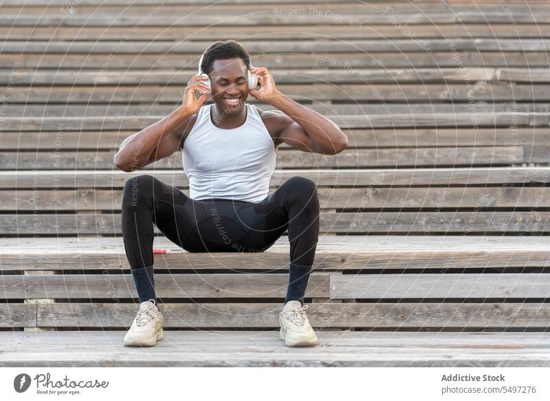 Schwarzer Sportler mit Kopfhörern, der auf einer Treppe Musik hört Athlet zuhören Gesang Sportbekleidung sich[Akk] entspannen schlank männlich schwarz