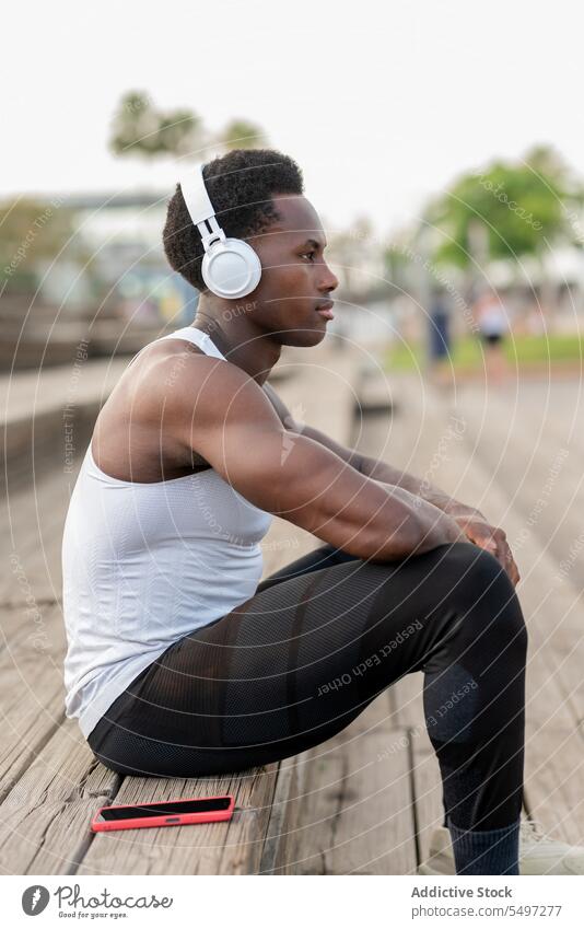 Begeisterter schwarzer Sportler mit Kopfhörern, der Musik genießt Athlet zuhören Gesang Smartphone Treppenhaus Porträt männlich Afroamerikaner Model passen