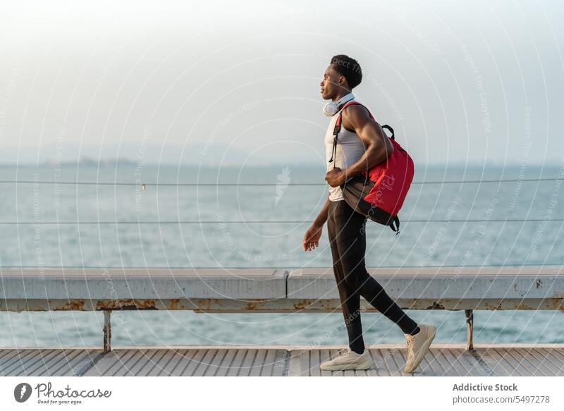 Schwarzer Mann mit Rucksack und Kopfhörern am Meer Stauanlage Spaziergang MEER Wasser Tasche Hafengebiet Gerät Strandpromenade männlich Afroamerikaner schwarz