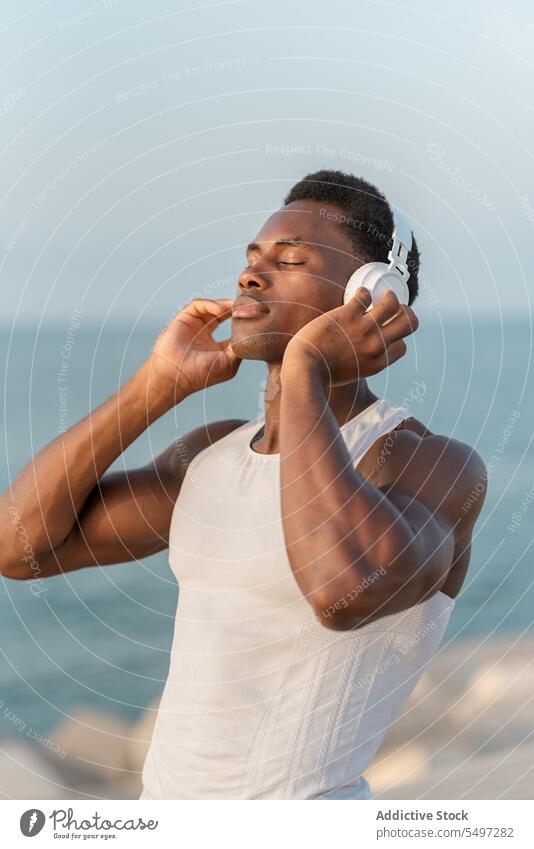 Nachdenklicher schwarzer Mann mit Kopfhörern am Meer Musik zuhören besinnlich MEER Gesang Drahtlos Klang Gerät männlich Wasser Melodie Windstille ruhig