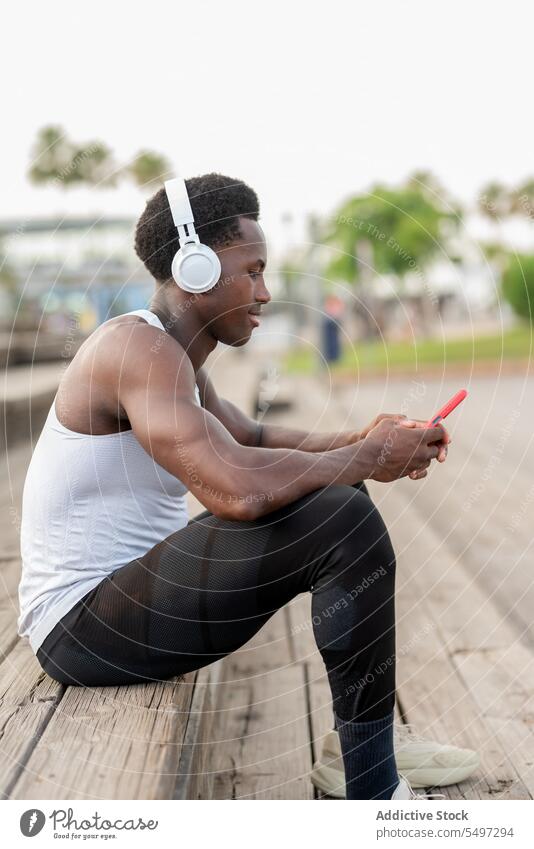 Begeisterter schwarzer Sportler mit Kopfhörern und Smartphone beim Musikgenuss Athlet zuhören Gesang Textnachricht Treppenhaus Porträt männlich Afroamerikaner