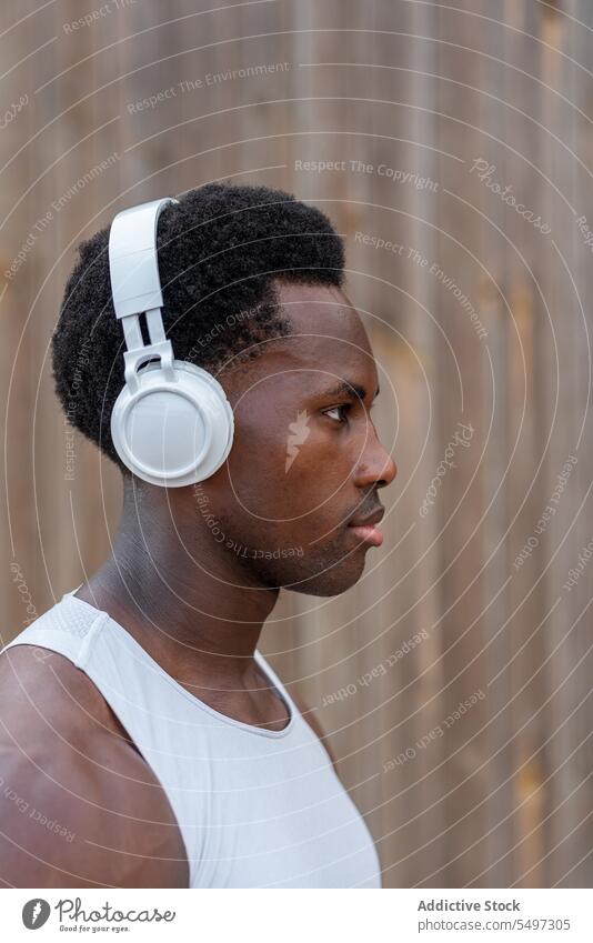 Fit junger afroamerikanischer Sportler mit Kopfhörern in der Nähe einer Holzwand Mann zuhören Musik Training Athlet angezogen selbstbewusst Porträt Kraft